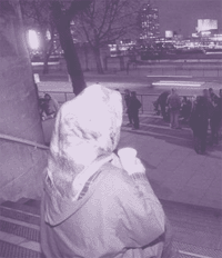 Photograph of an older homeless woman looking across a crowded street at night